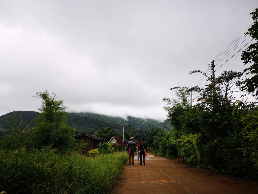 Andrew Murphy and Suriya Kalasin walking down a village road toward cloud-covered mountains in northern Thailand
